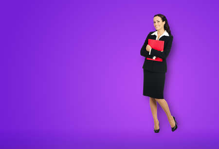 Full body length of happy smiling businesswoman holding red folder, copy space area for text. Confident business woman in black suit standing over violet purple background.の写真素材