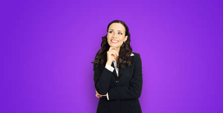 Happy smiling amazed positive businesswoman looking up, with copy space for slogan or text. Confident brunette business woman in black suit, violet purple background.の写真素材
