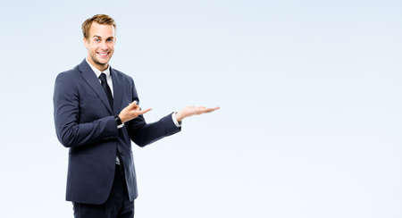 Businessman in suit showing, holding, giving some product or copy space area for advertising text, isolated on grey background. Young happy corporate business man at studio image. Professional person.の写真素材