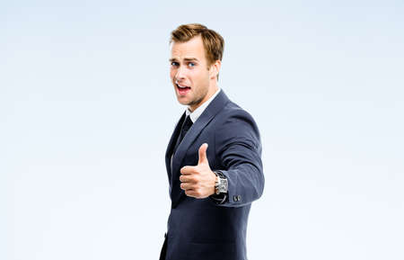 Happy businessman in black suit, white shirt, necktie show thumb finger up, like, agree hand gesture, isolated on grey background. Representative business man at studio image. Success concept.の写真素材