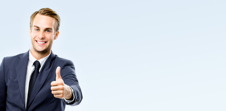 Happy smiling businessman in black suit, white shirt, tie show thumb up, like, agree hand gesture, isolated on grey background. Representative business man at studio image. Success concept. Copy spaceの写真素材