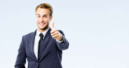 Happy businessman in black suit, white shirt, necktie show thumb finger up, like, agree hand gesture, isolated on grey background. Excited young business man at studio image. Success ad concept.の写真素材