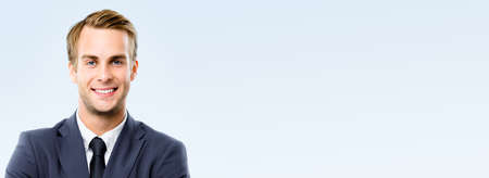 Portrait image of smiling confident businessman in black suit, tie, isolated over grey background. Representative business man at studio. Copy space text area. Wide banner compositionの写真素材