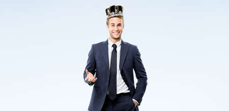 Portrait image of excited happy smiling business man in fake crown on his head, isolated over grey background. Young businessman at leadership success studio advertisement concept.の写真素材