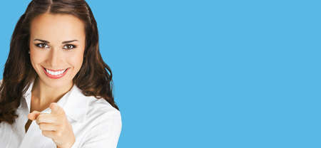 What about You? Happy smiling woman in white confident blouse pointing finger at viewer, copy space. Business concept. Isolated on blue color background. Brunette businesswoman. Wide.の写真素材