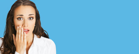 Unbelievable news! Excited surprised, shocked businesswoman. Business woman covering open mouth by her hand. Isolated over blue background. Wide banner composition.の写真素材