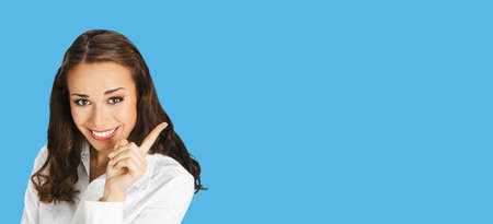 Close up portrait of happy smiling woman in white confident blouse, showing pointing at copy space for text. Business concept. Isolated over blue background. Brunette businesswoman. Wide image.の写真素材