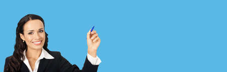 Portrait of happy smiling beautiful young businesswoman in black confident suit, writing or drawing something on screen, by marker. Brunette woman, isolated on blue backgroundの写真素材