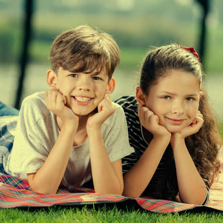 Two happy smiling children, laying on picnic blanket, outside. Childhood and summer time concept. Square composition image.の写真素材