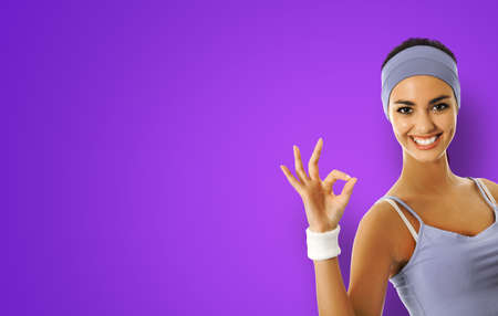 Young happy african american woman in sportswear showing okay ok hand sign gesture, isolated on violet purple background. Sporty model at studio shot. Fitness concept.の写真素材