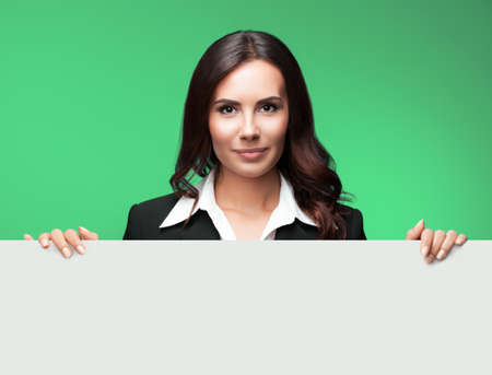 Portrait image of happy smiling young business woman in black suit, showing white signboard with blank copy space area for text, isolated on green background.の写真素材