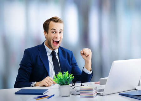 I have done it! Very happy businessman in blue suit, working with laptop. Success in business job and concept image. Cheerful business man at office workplace.の写真素材