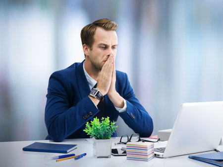 Stressed or hardly thinking businessman in blue suit, working with laptop at office. Business, job and education concept image.の写真素材