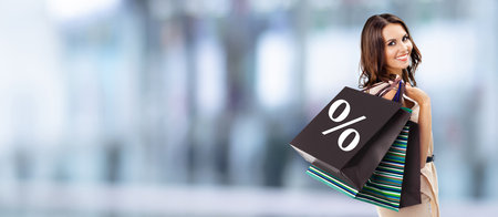 Shopping woman. Happy girl holding grocery bags with % sign, blurred mall background. Copy space for ad slogan or some text. Big deals, discounts offers, Black Friday holidays sales concept picture.の写真素材