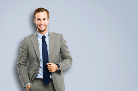 Portrait of happy confident businessman in grey suit, blue shirt and tie, isolated over grey background. Business success concept. Smiling man at studio picture.の写真素材