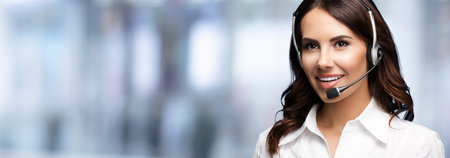Call Center Service. Beautiful young customer support or sales female agent. Caller or receptionist phone operator. Help, answering, consulting. Against blurred office background. Copy space area.の写真素材