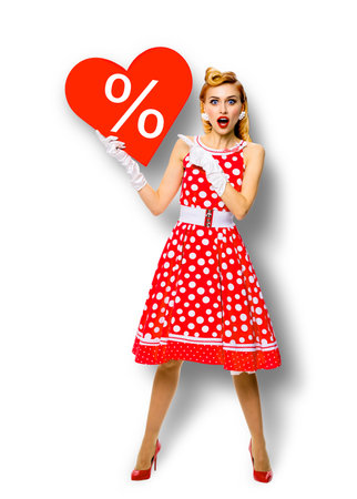 Woman holding red paper heart shape with % sign. Full length body portrait of happy pin up girl showig pointing signboard. Sales ad concept. Isolated on white background. Valentine or like symbolの写真素材