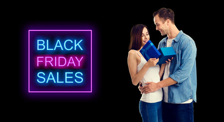 Big deals, discounts offers concept - happy smiling amorous couple opening gift box. Black Friday Sales sign text.の写真素材