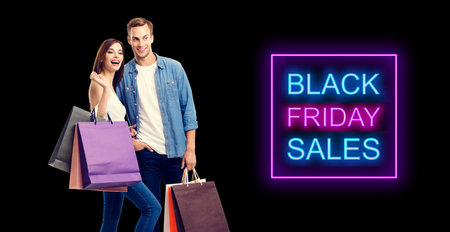 Big deals, discounts offers concept - happy excited laughing couple with shopping bags. Isolated over dark background. Black friday sales neon light sign text.の写真素材
