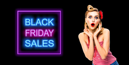 Unbelievable deals! Excited surprised, very happy woman. Pin up syle girl with open mouth and raising hands. Retro and vintage studio ad concept. Black Friday sales neon light sign.の写真素材