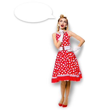 Full body length image of thinking woman in red pin up dress. Blond pinup thougthfull girl in studio, isolated white background. Empty blank speech sign bubble, having idea.の写真素材