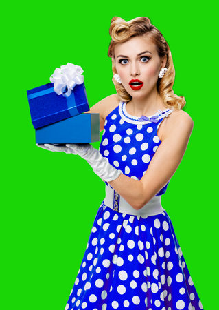 Image of beautiful woman dressed in pin up dress with polka dot opening gift box, isolated on green chroma key background. Blond pinup model - big sales ad studio concept.の写真素材