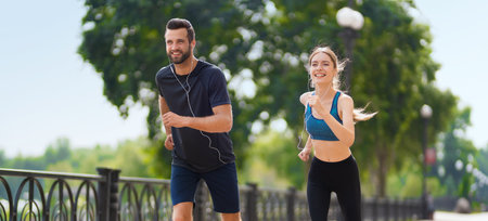 Morning jogging. Wide image of happy smiling young couple, runners running together, woman train with man, or bearded fit coach exercising outdoors. Fitness, sport city marathon workout concept.の写真素材