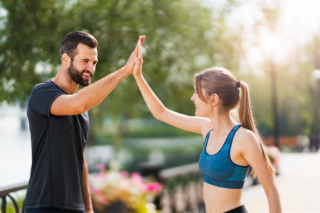 Image of happy smiling couple giving highfive, high five hands gesture, woman with man or bearded coach trainer, clapping palms, after successful training, outdoors. Fitness, sport, workout concept.の写真素材