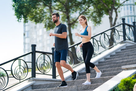 Image of happy smiling young couple, runners walking down or running on stone stairs, woman train with man, or bearded fit coach exercising, outdoors. Fitness, sport city, morning workout concept.の写真素材