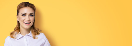 Wide banner composition image of happy smiling businesswoman, with copy space area for some slogan or text. Confident woman in white shirt, isolated on orange yellow background. Business concept.の写真素材