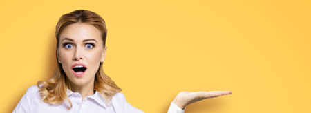 Portrait of very happy, excited surprised, astonished businesswoman with wide opened eyes, mouth, showing copy space text area. Success in business concept. Orange yellow background.の写真素材