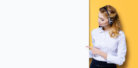 Call Center Service concept - customer support or sales agent. Businesswoman, caller, receptionist, phone operator pointing at empty sign board. Helping consulting. Orange yellow background.の写真素材