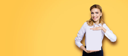 Cheerful smiling business woman in white confident clothing showing empty mock up signboard. Success and advertising concept. Copy space place for text, orange yellow background.の写真素材