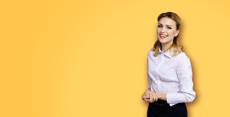 Happy smiling attractive businesswoman, with copy space area for some slogan or text. Confident blond woman in white shirt, on orange yellow background. Business concept.の写真素材