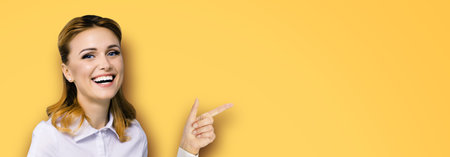 Very happy, excited confident woman, showing pointing finger at copy space empty text area. Success in business ad concept. Orange yellow background. Wide horizontal banner composition.の写真素材