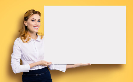 Happy excited smiling business woman in white confident clothing showing blank banner signboard. Success and advertising concept. Copy space empty place for some text. Orange yellow background.の写真素材