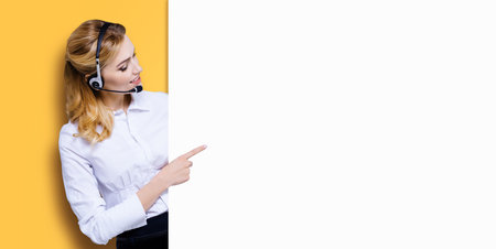 Call Center Service concept - customer support or sales agent. Businesswoman, caller, phone operator pointing finger at signboard with copy space. Help, answering, consulting. Orange yellow backgroundの写真素材