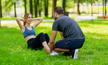 Image of young smiling couple, woman training with man or bearded coach trainer, doing twist fit exercise together, look at each other, outdoors. Fitness, sport, workout, healthy lifestyle concept.の写真素材