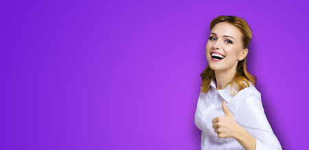 Excited happy smiling businesswoman, showing thumb finger up or like hand sign gesture. Success in business studio concept. Isolated on violet purple background.の写真素材