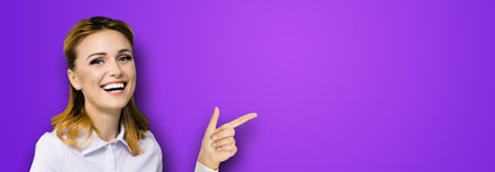 Very happy, excited confident woman, showing pointing finger at copy space empty text area. Success in business ad concept. Violet purple background. Wide horizontal banner compositionの写真素材