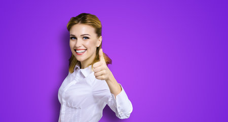 Excited happy smiling businesswoman, showing thumb finger up or like hand gesture. Success in business studio concept. Isolated on violet purple background.の写真素材