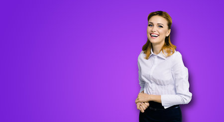 Happy smiling attractive businesswoman, with copy space area for some slogan or text. Confident blond woman in white shirt, violet purple color background. Business concept.の写真素材