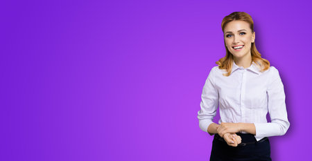 Happy smiling attractive businesswoman, with copy space area for some slogan or text. Confident blond woman in white shirt standing over violet purple background. Business conceptの写真素材