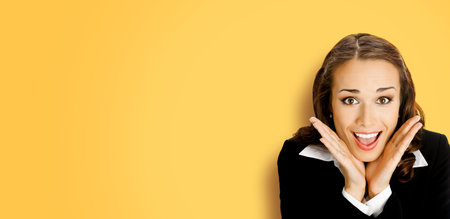 Unbelievable news! Excited surprised, shocked businesswoman. Business woman with open mouth, hands near face, over copy space, against yellow.の写真素材