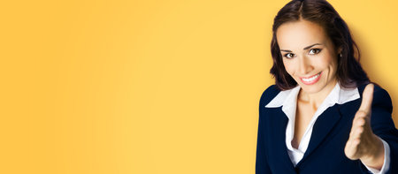 Businesswoman in confident black suit giving hand for handshake, copy space place for text, advertising or slogan, on yellow color background. Business studio concept.の写真素材
