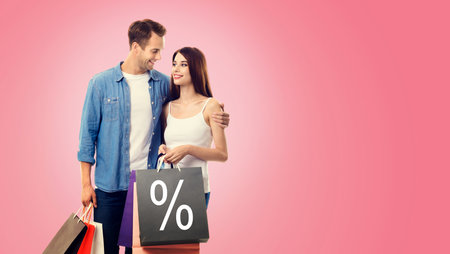Holiday sales actions, rebates, discounts offers concept image - happy couple with shopping bags, looking at each other, isolated on vivid rose pink background. Copy space. % signの写真素材