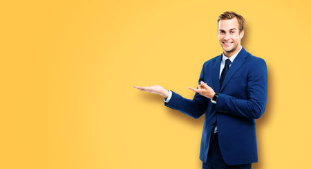 Businessman showing giving advertising something, isolated on vivid yellow colour background. Copy space for some slogan or text message. Success in business education ad concept.の写真素材