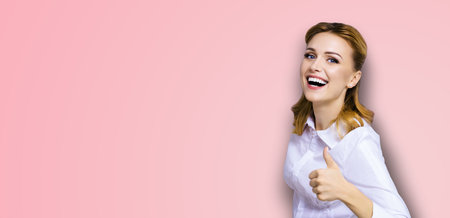 Excited happy smiling businesswoman, showing thumb finger up or like hand sign gesture. Success in business studio concept. Isolated on rose pink background.の写真素材