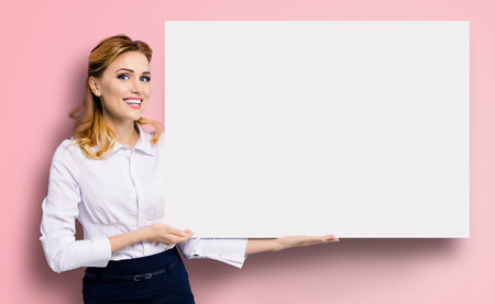 Happy excited smiling business woman in white confident clothing showing blank banner signboard. Success and advertising concept. Copy space empty place for some text. Rose pink background.の写真素材