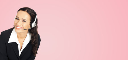 Call center service. Portrait image of female customer support phone sales operator in headset showing something or copy space area for text or slogan, over rose pink background.の写真素材